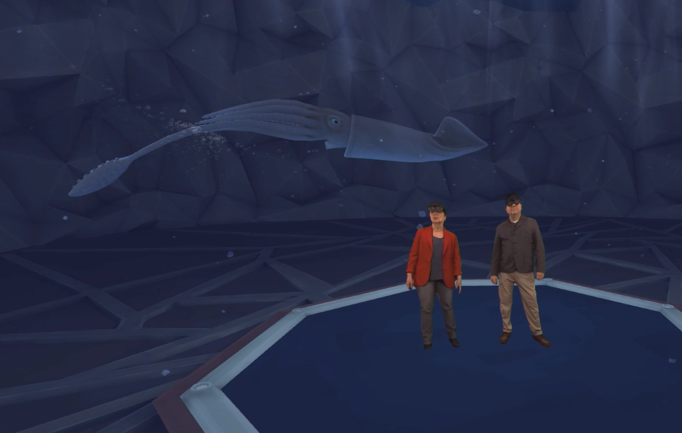 Video screenshot from Ignite keynote shows OceanX presenters standing near a projection of a giant squid.