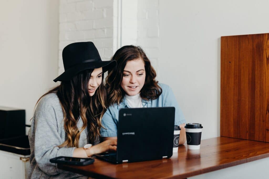 Photo shows two women amused looking at a laptop together.